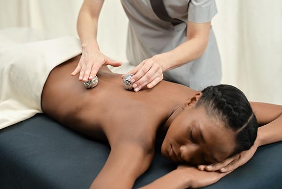 Person lying on their front having two silver spheres rolled on their back