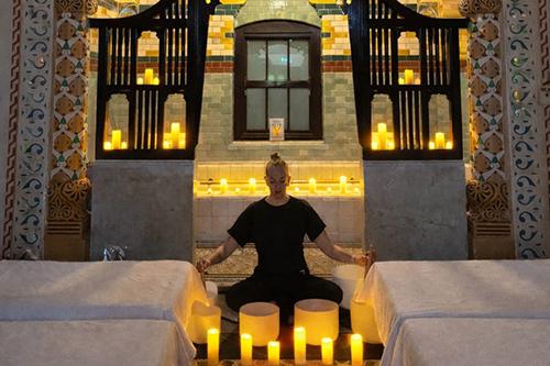 Adult sitting on the floor inside the Turkish Baths with lit candles around them.